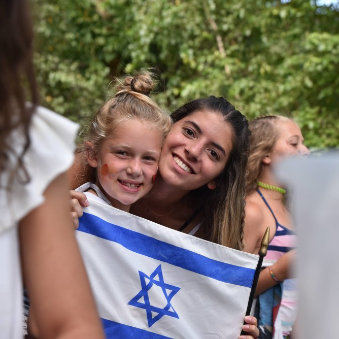 A staff member and camper holding an Israeli flag.