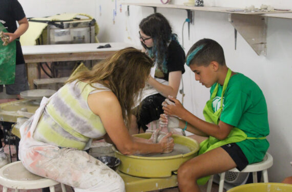 A camper and staff member working on pottery.