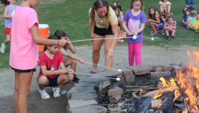 Campers toasting marshmallows in front of a camp fire.