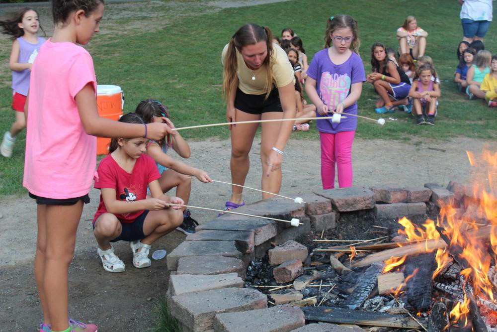 Campers toasting marshmallows in front of a camp fire.